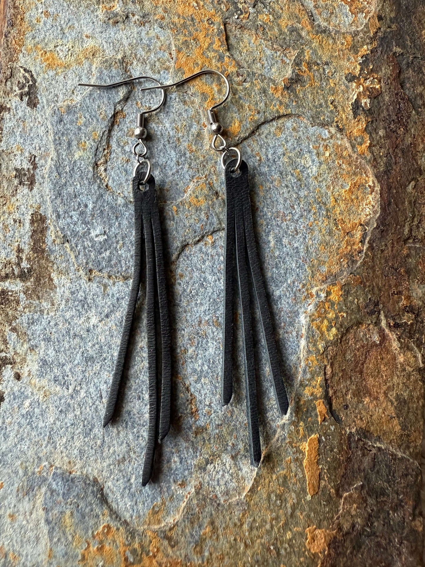 Pair of black leather fringe earrings on a textured stone surface