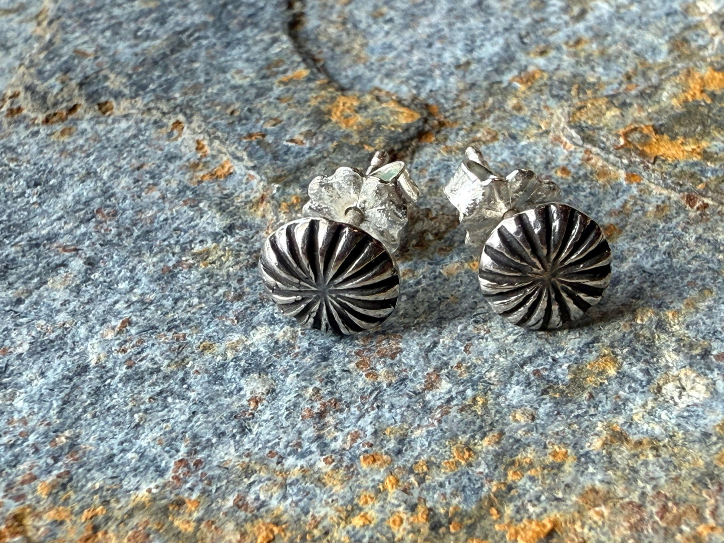 Silver starburst earrings on a textured stone surface