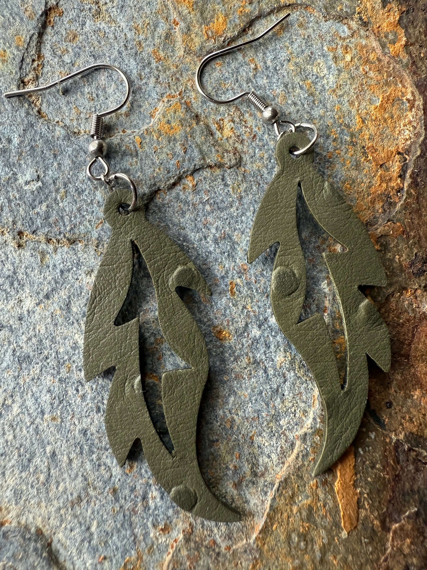 Green feather-shaped earrings on a textured stone surface
