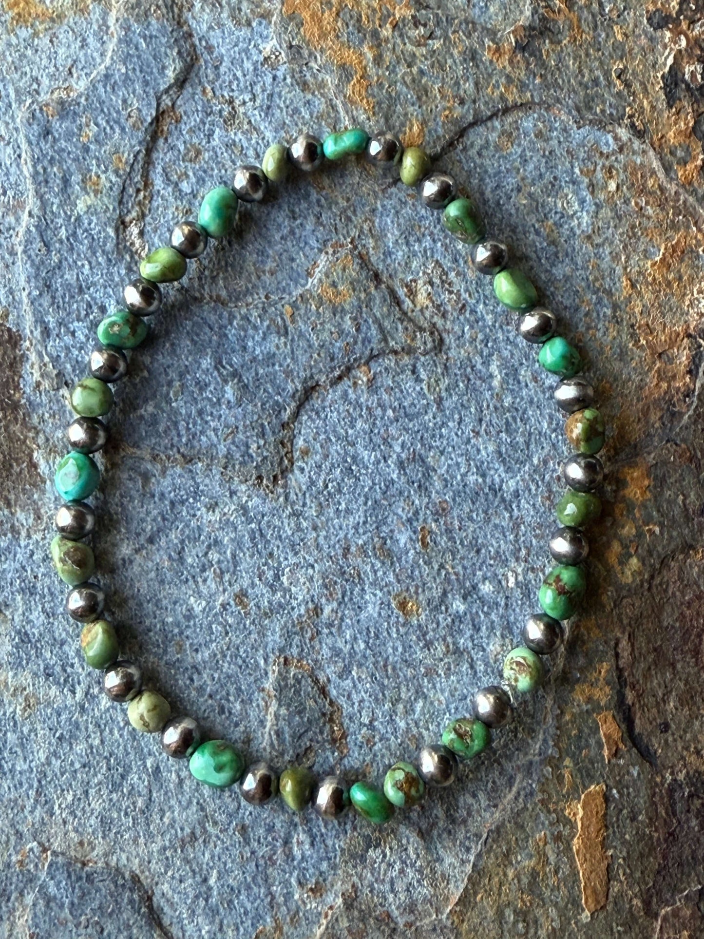 Sonoran Gold Turquoise Sterling Silver Pearl Bracelet displayed on a textured stone surface, showcasing vibrant turquoise and silver elements.
