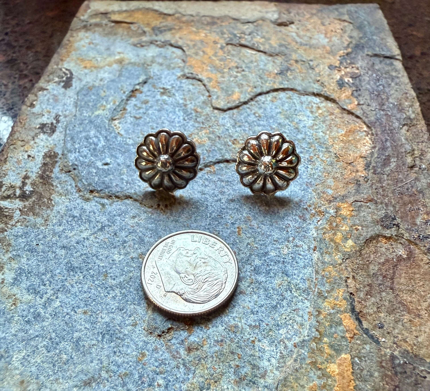 Silver Rustic Flower Concho Post Earrings displayed with a quarter for size comparison on a textured stone surface.
