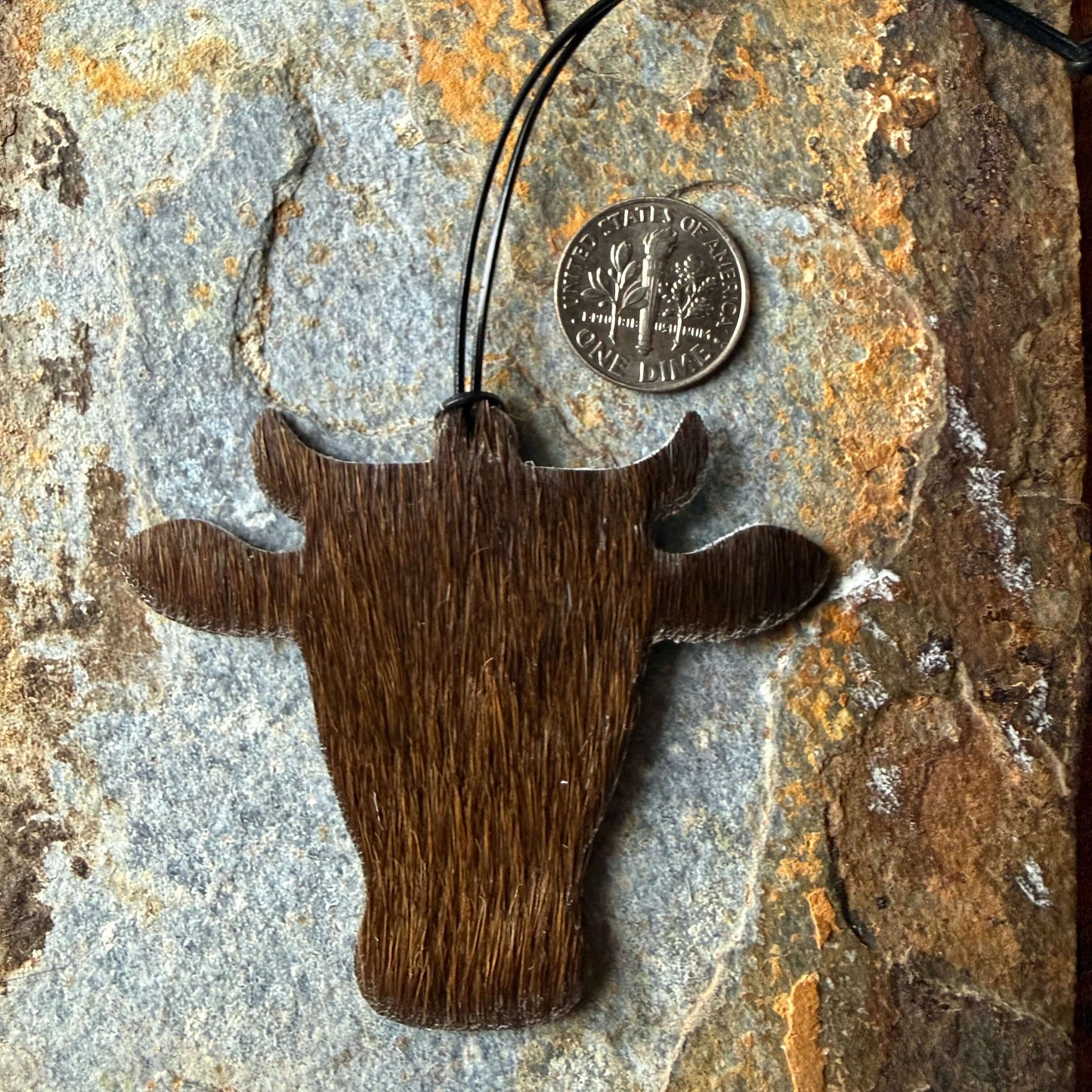 cowhide ornament shaped like a bull head on a textured stone surface with a coin for scale.