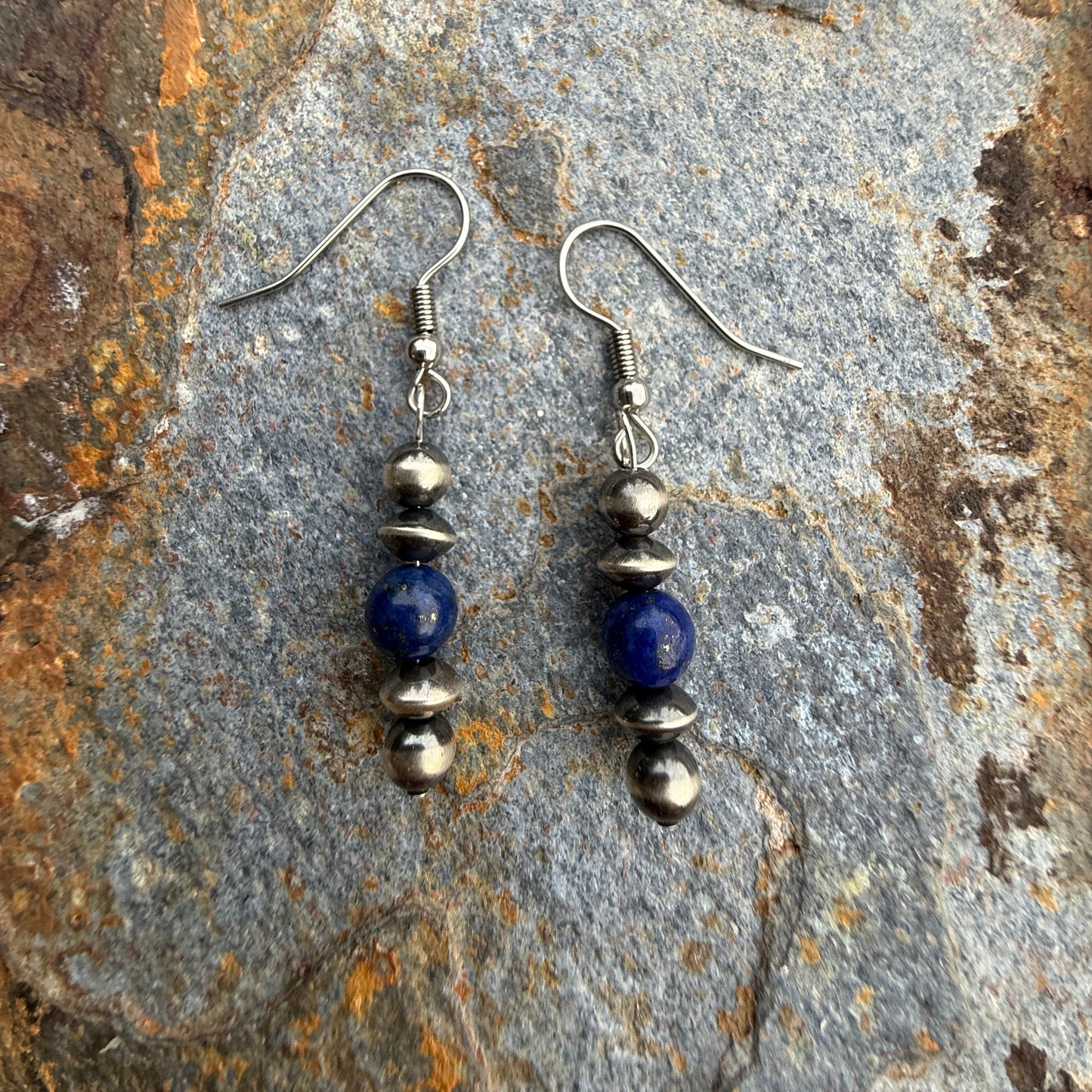 Pair of silver and blue beaded earrings on a textured stone surface