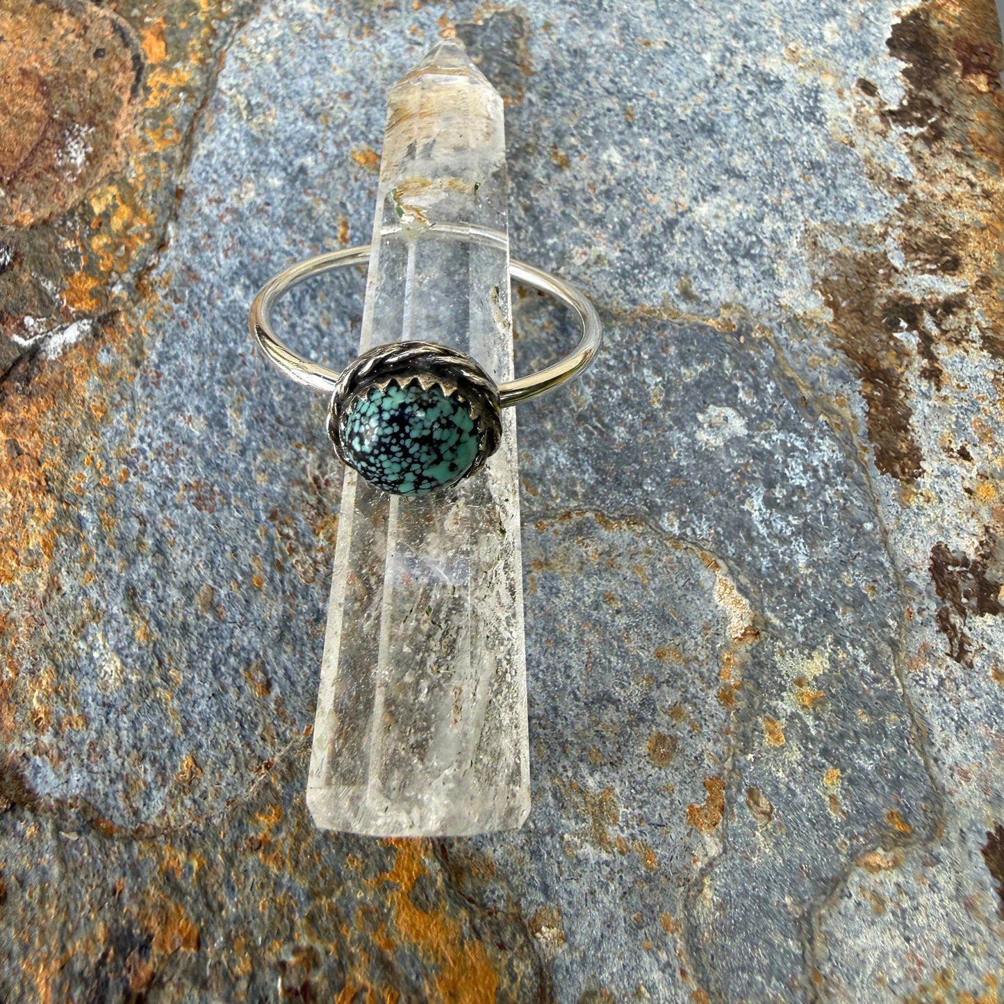 Ring with a dark green gemstone on a clear stand, placed on a textured stone surface.