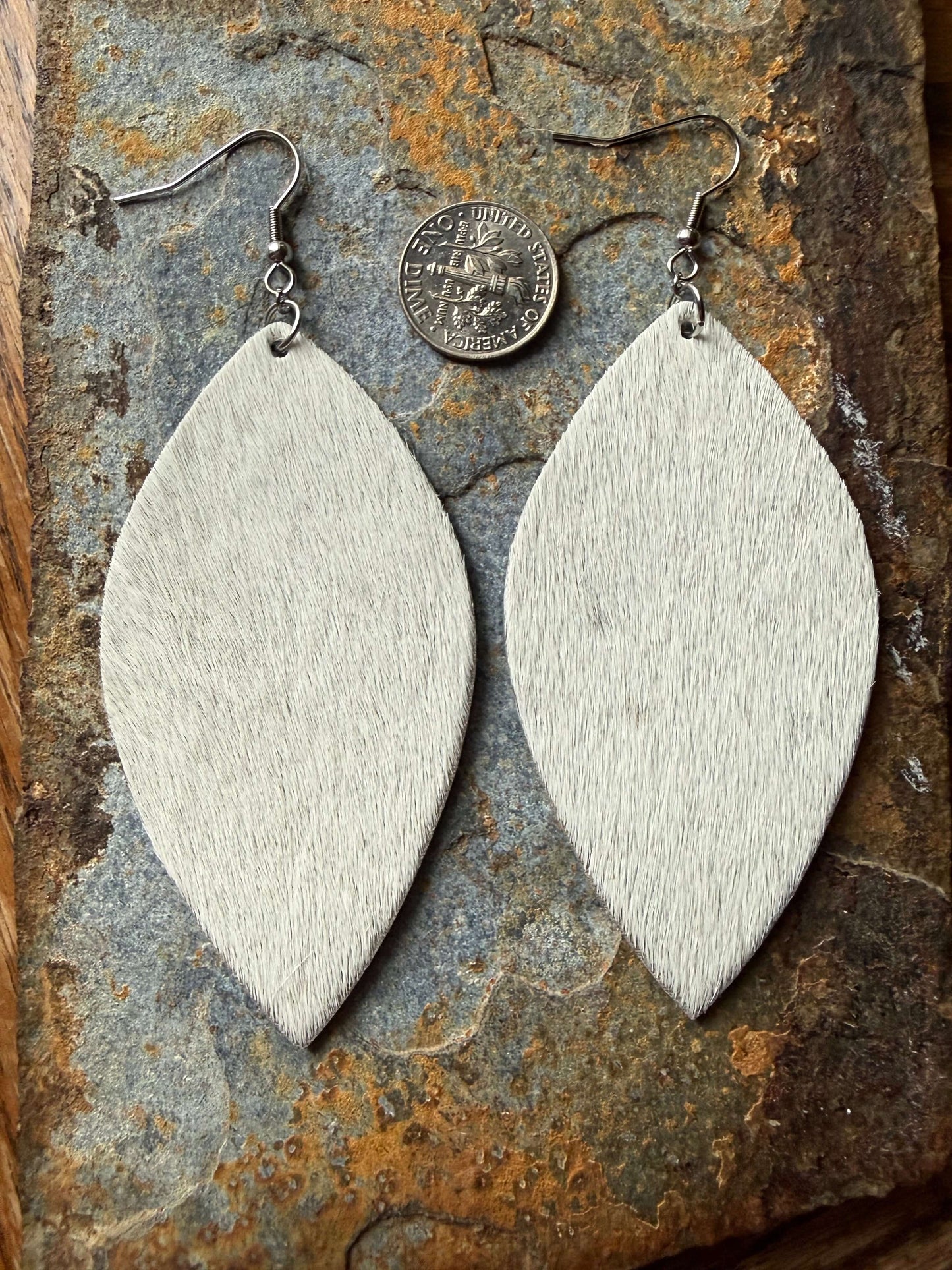 Cowhide Large Leaf Earrings displayed on natural stone background alongside a coin for scale.