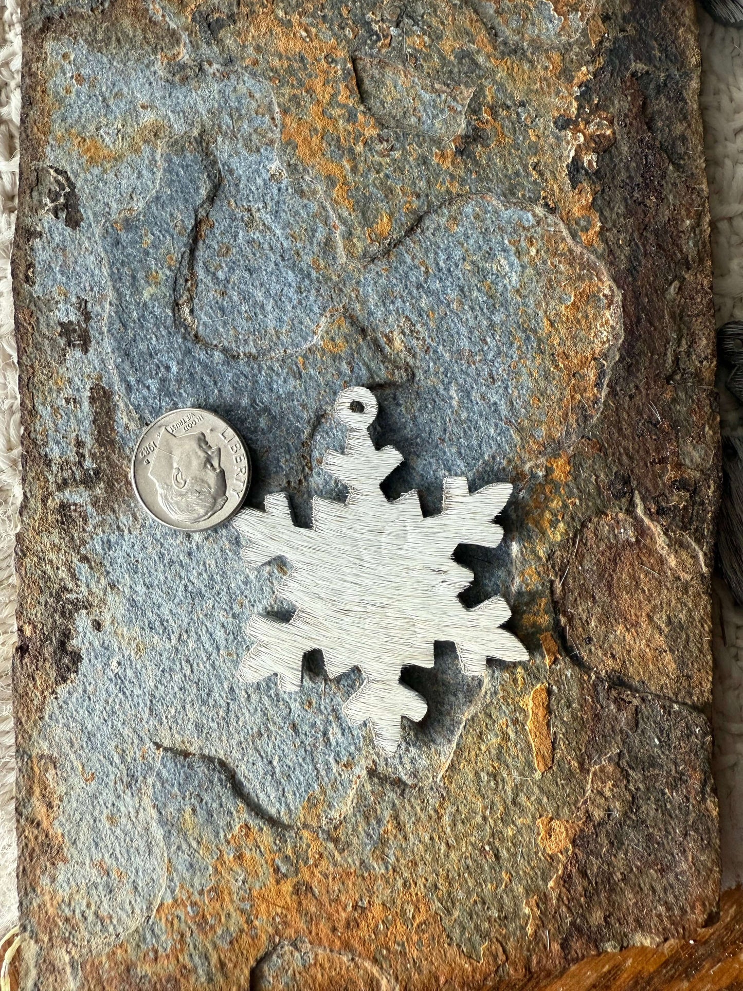 Hair on cowhide mini snowflake ornamentsHair on cowhide mini snowflake ornaments on rustic stone background with quarter for size reference.