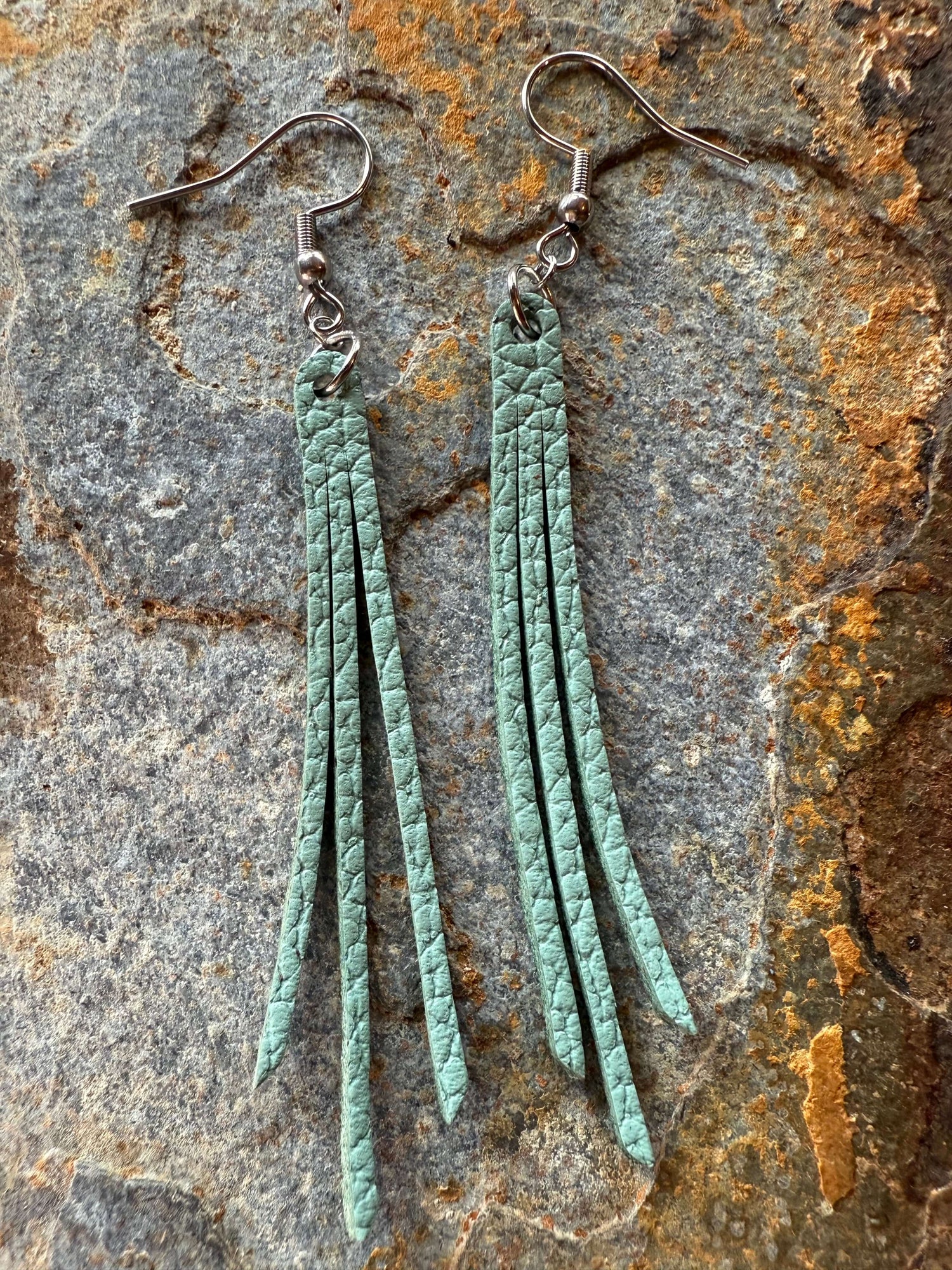 Pair of turquoise leather fringe earrings on a textured stone surface