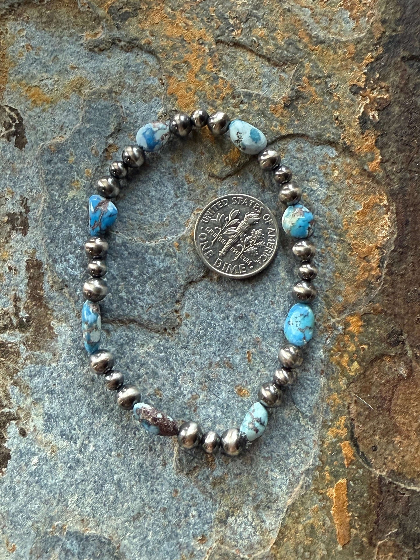 Golden Hills Turquoise Pearl Bracelet featuring turquoise beads and silver accents, elegantly displayed on a textured surface.
