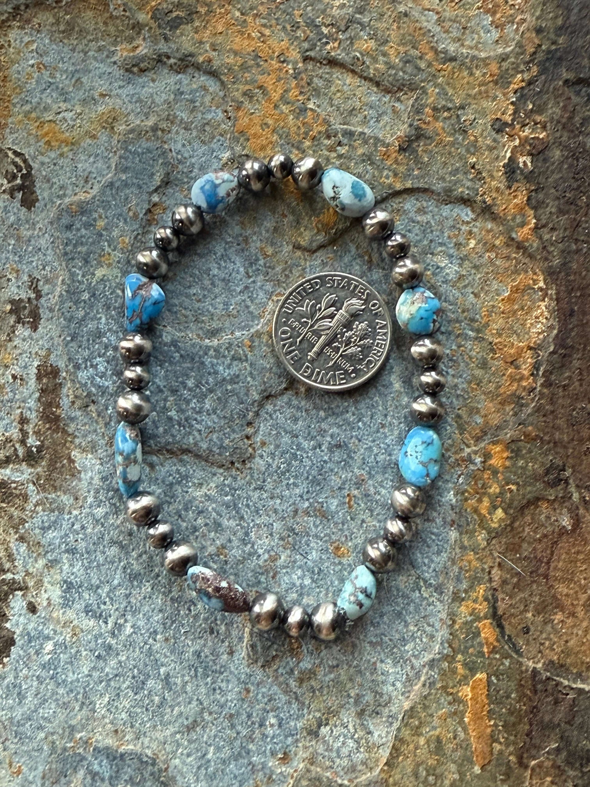 Golden Hills Turquoise Pearl Bracelet featuring turquoise beads and silver accents, elegantly displayed on a textured surface.