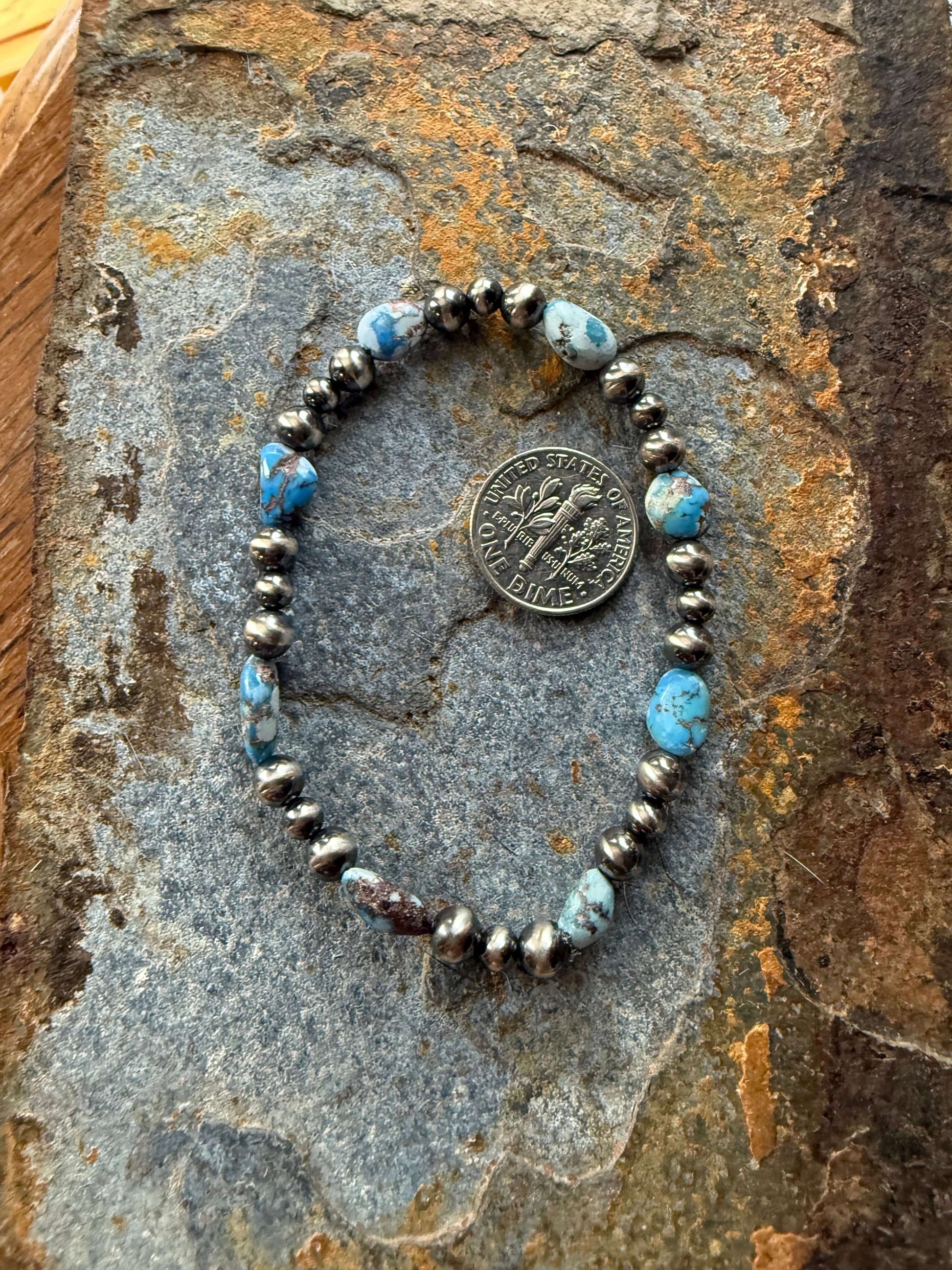 Golden Hills Turquoise Pearl Bracelet featuring blue turquoise stones and silver beads on a textured stone background.