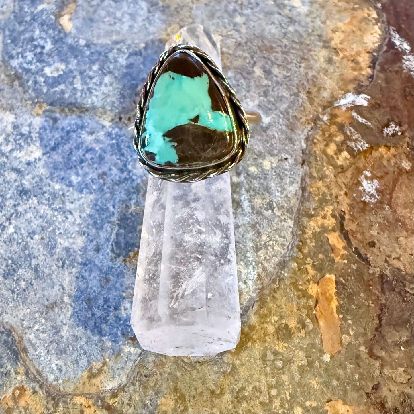 Ring with a turquoise stone on a crystal base against a natural stone background