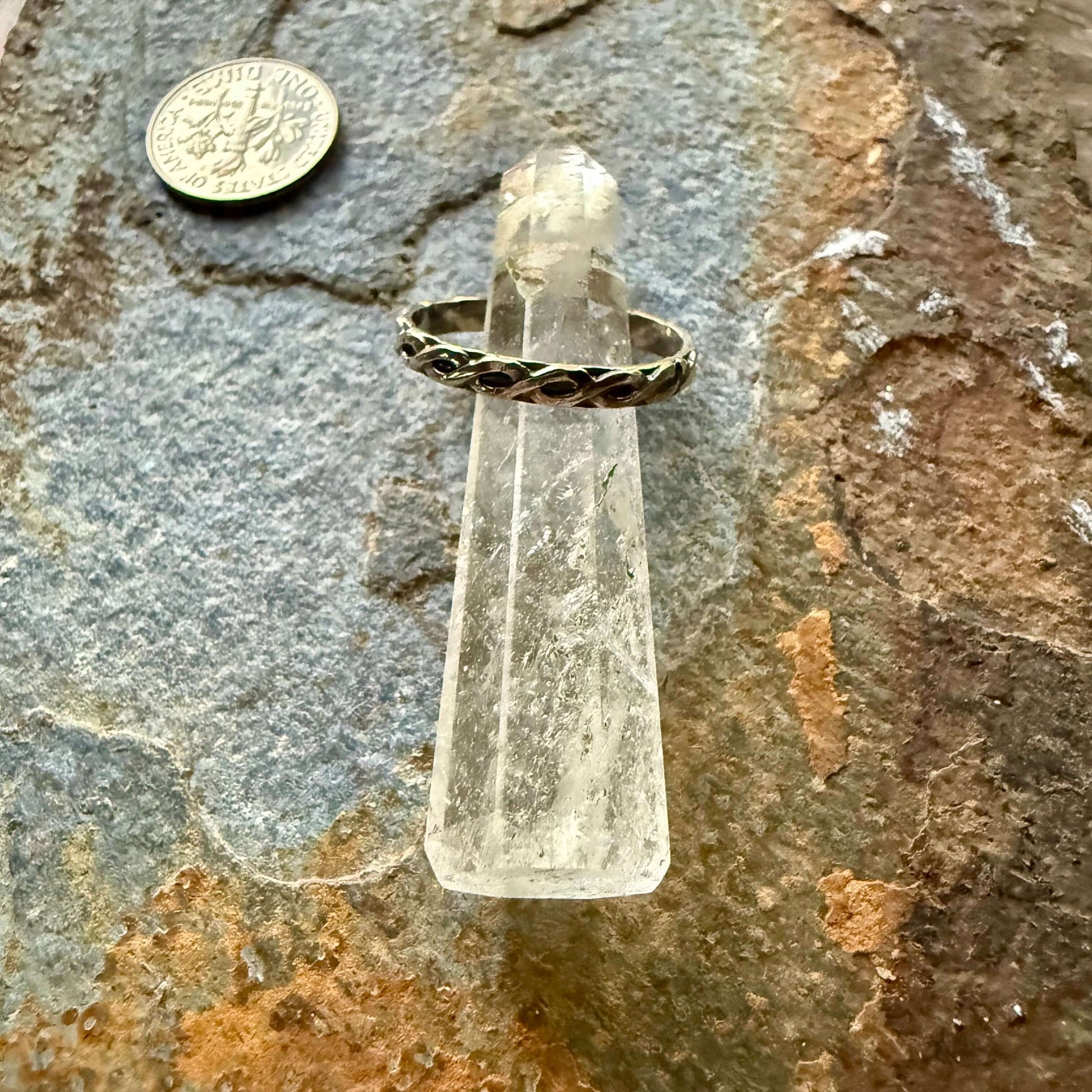 Gold ring on a clear crystal with a coin for scale on a stone surface