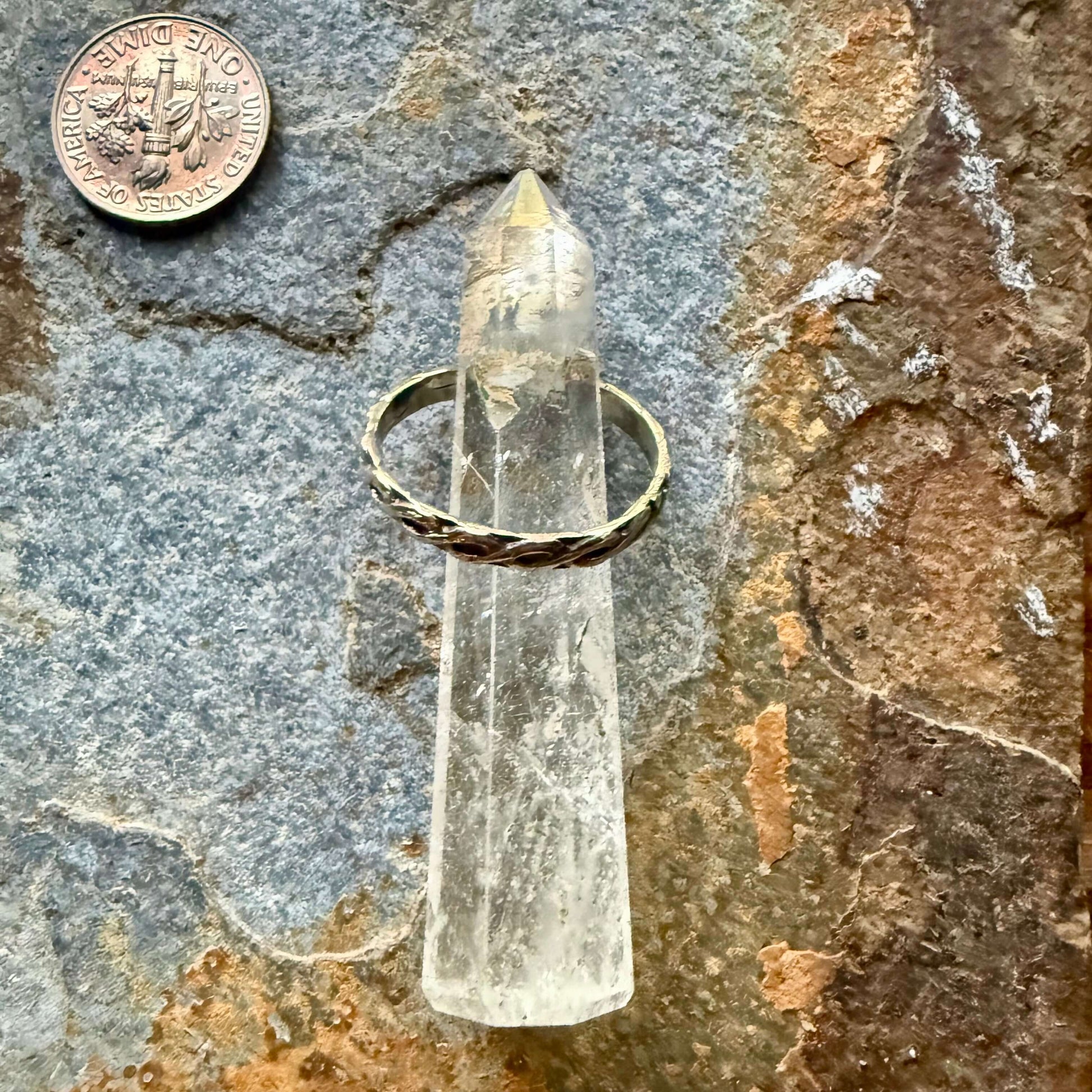 Clear crystal point with gold ring on a textured stone surface, coin for scale