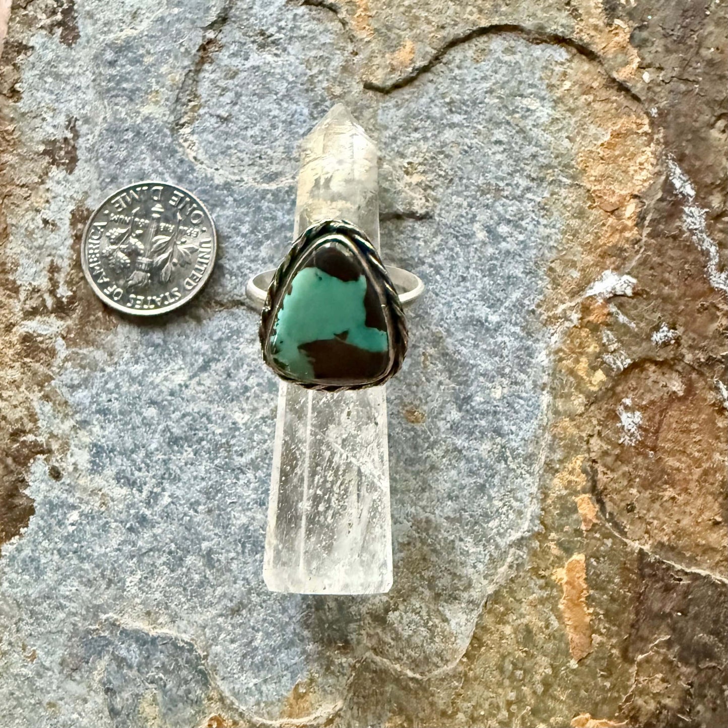 Turquoise ring on a clear crystal with a coin for scale on a stone background