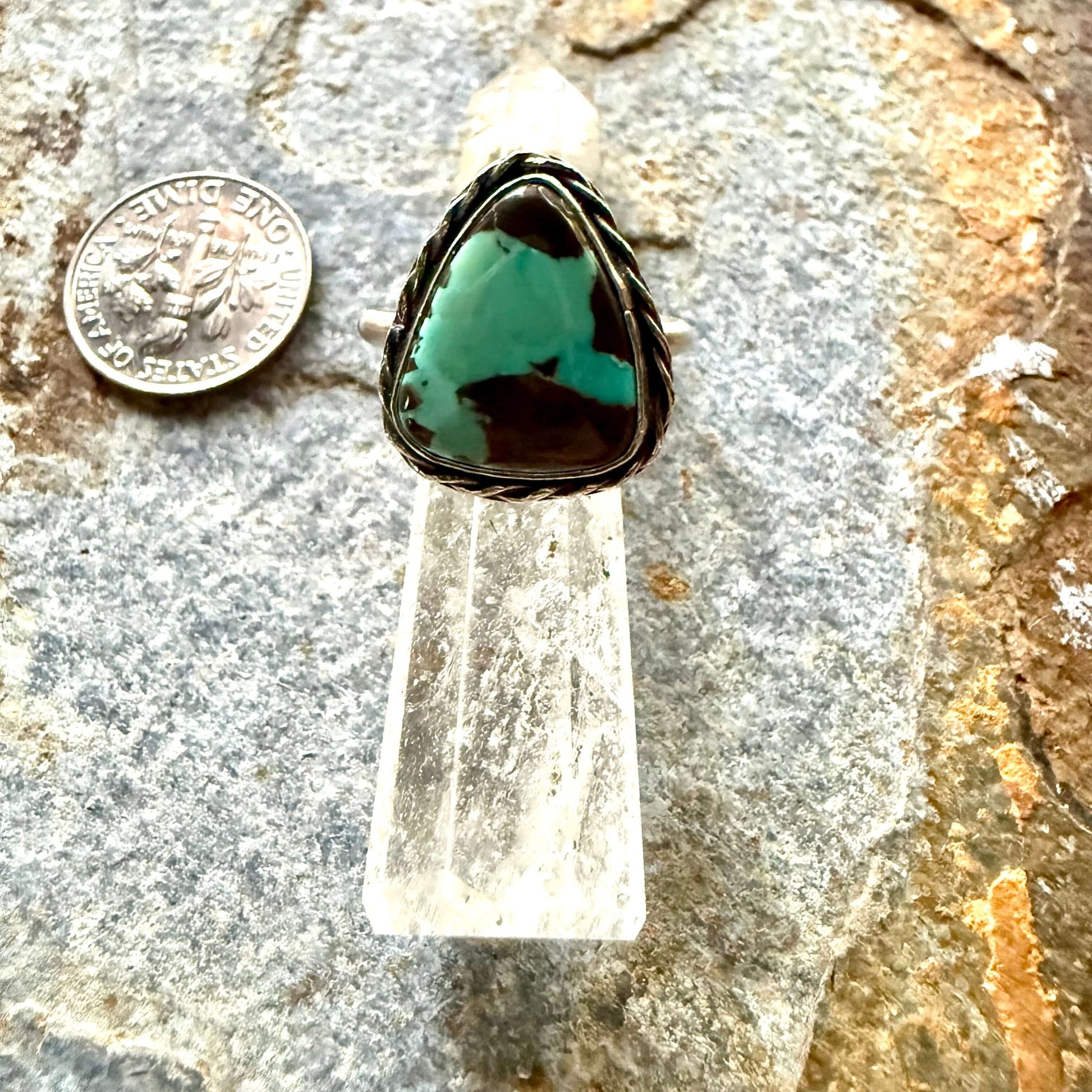 Turquoise stone with silver setting on a rock surface next to a coin for scale.
