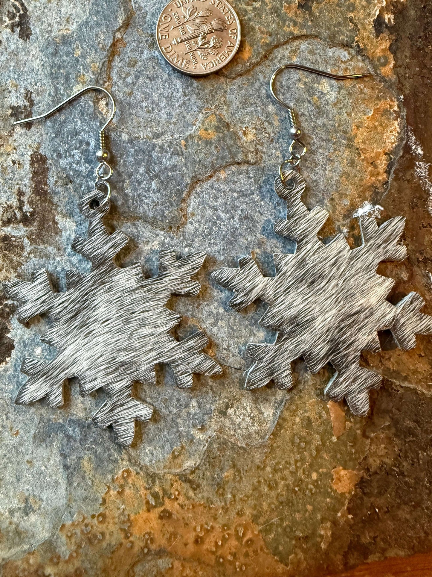 Cowhide Snowflake Earrings on a stone surface next to a coin, showcasing rustic Western charm and elegant design.