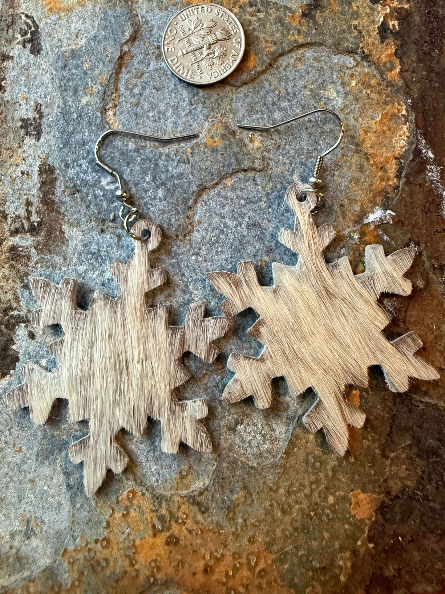 Cowhide Snowflake Earrings on rustic background with a coin for scale, showcasing Western charm and elegance.