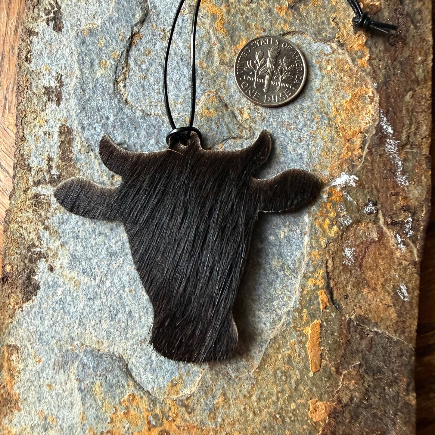 cowhide ornament shaped like a bull head on a textured stone surface with a coin for scale.