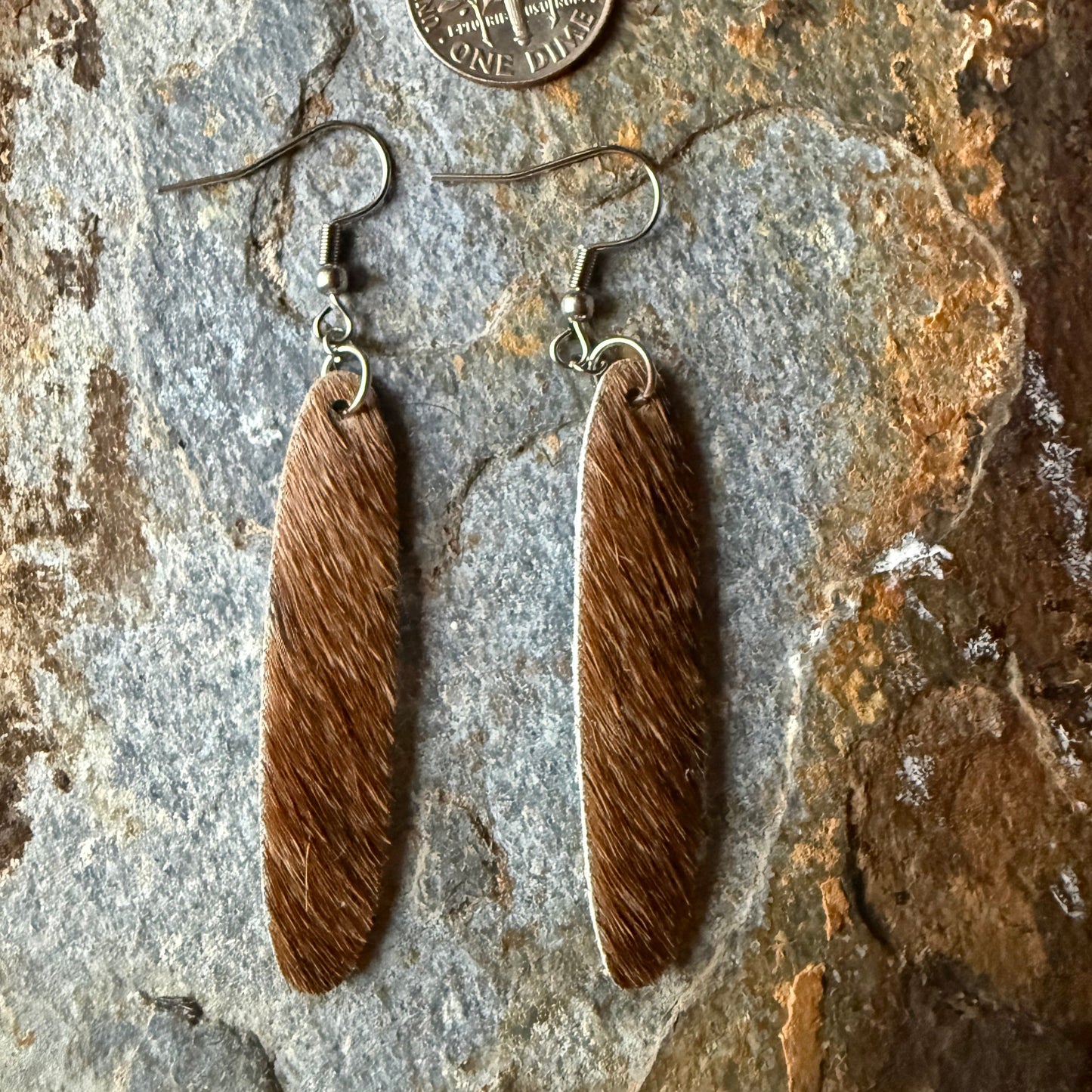 Cowhide oval shaped earrings on a stone surface