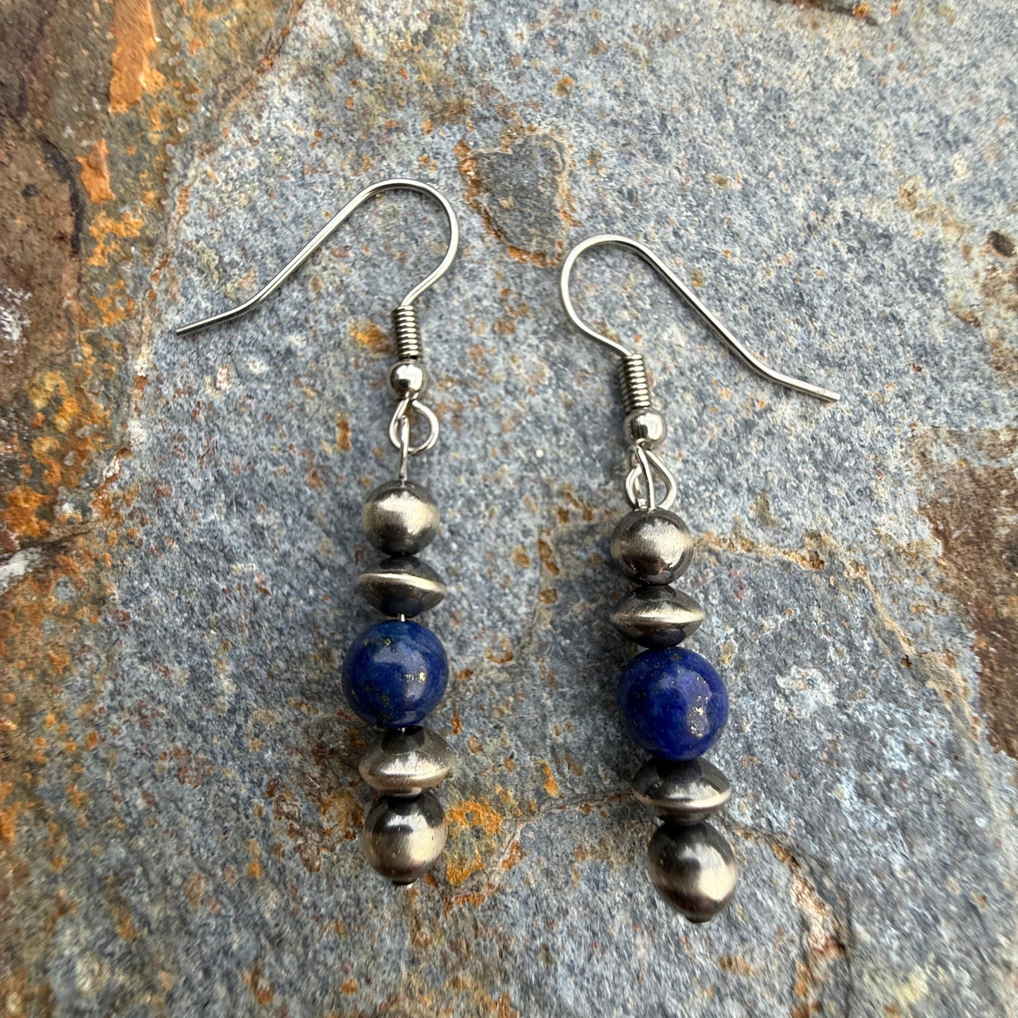 Pair of beaded earrings with blue and silver beads on a stone surface
