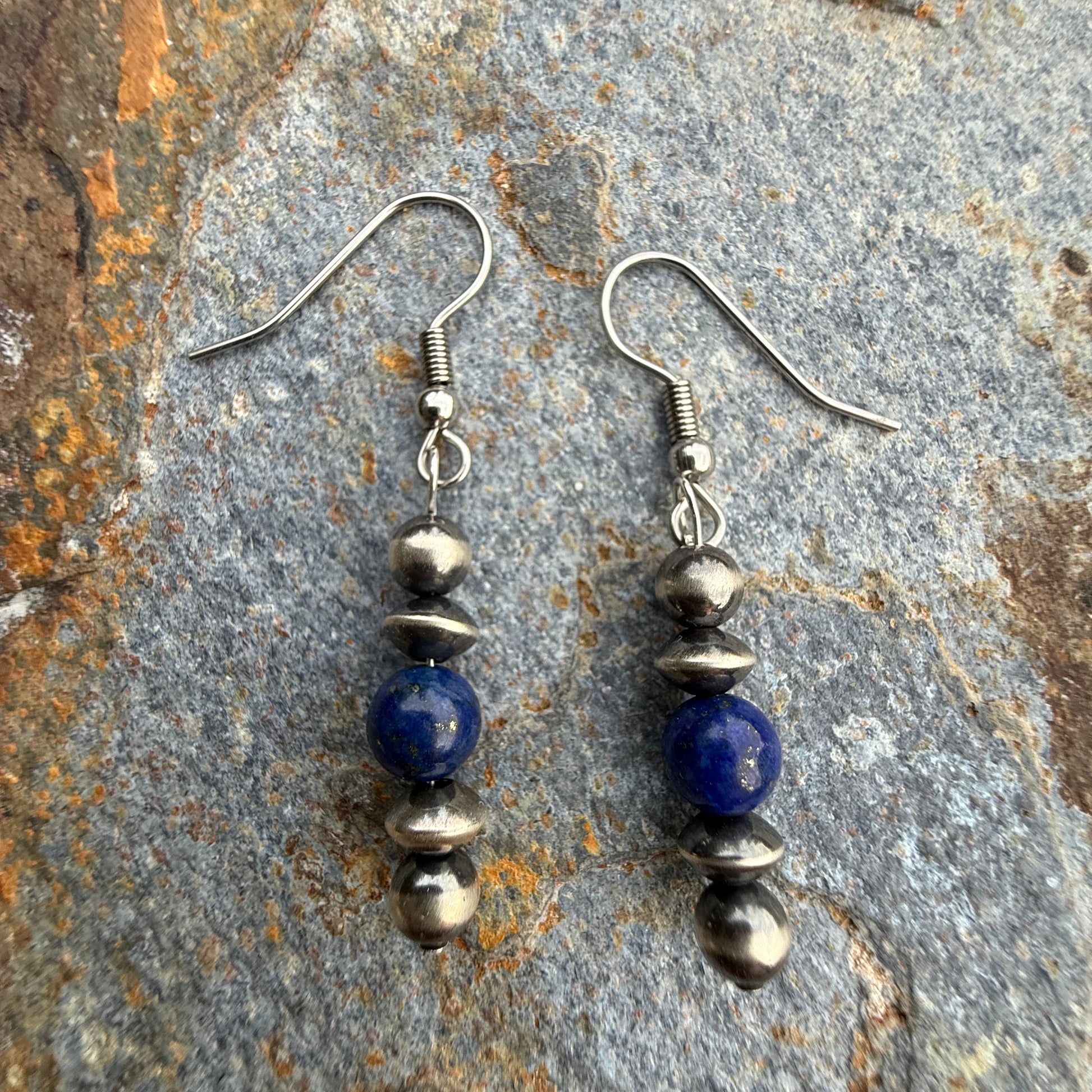 Pair of beaded earrings with blue and silver beads on a stone surface