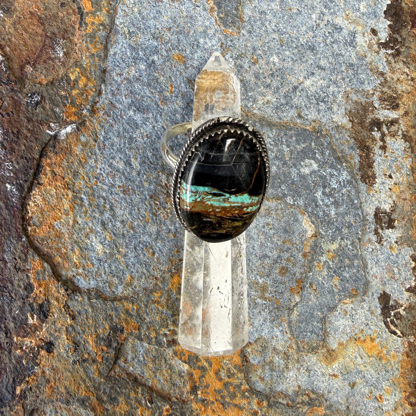 Silver ring with a black stone on a textured rock surface
